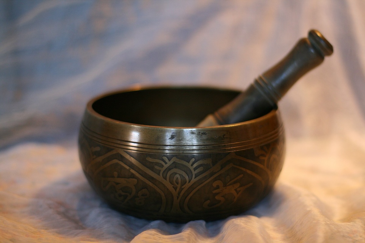 A dark engraved singing bowl with its striker, on a soft cloth